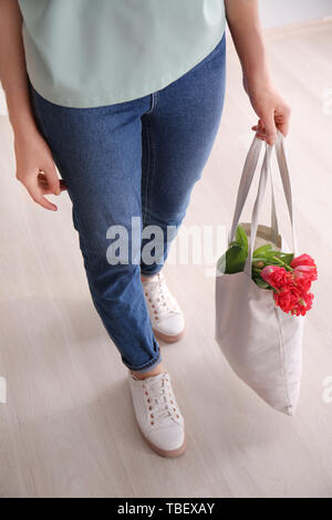 Donna che mantiene eco borsa con fiori in ambienti interni Foto Stock