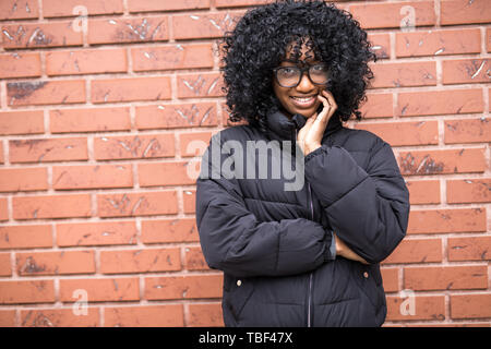 Ritratto di giovane curly donna africana in piedi di fronte a un muro di mattoni. Foto Stock