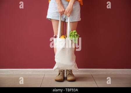 Giovane donna con verdure in sacchetto eco vicino alla parete del colore Foto Stock