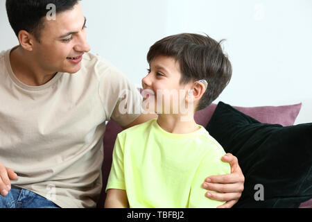 Giovane uomo e suo figlio con apparecchi acustici a casa Foto Stock