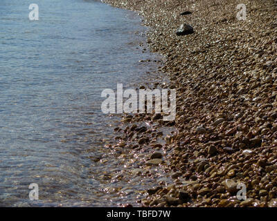 Mar Rosso costa ghiaiosa con pura acqua trasparente. Solar macchie di luce sono riflesse da pietre. Foto Stock