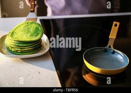 Donna mettendo appena fritte frittelle di verde su piastra in cucina Foto Stock