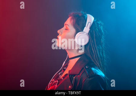 Godetevi, meloman e concetto di persone - una giovane donna con dreadlocks ascoltando la musica, ritratto su sfondo scuro Foto Stock