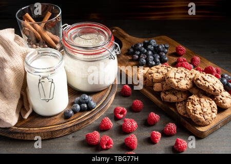 Latte, cinnamom, farina in contenitori sigillati, biscotti e bacche collocato su legno Foto Stock