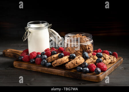 Biscotti, di bacche e di latte sul fondo in legno, vista laterale. Foto Stock