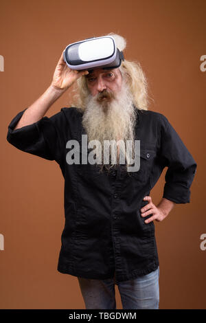 Studio shot di senior uomo barbuto che indossa la maglia nera contro lo sfondo marrone Foto Stock