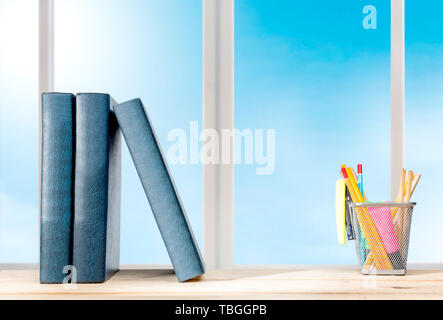 Pila di libri in piedi e matite in contenitore a cestello con cucitrice verde sul tavolo in legno con vetro di finestra di sfondo. Si torna a scuola concept Foto Stock