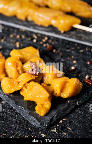 Primo piano di alcune spezie pollo crudo spiedini di carne e di alcuni cubetti di greggio speziata carne di pollo su due nero ardesia piastre, su un tessuto superficie nera, primavera Foto Stock