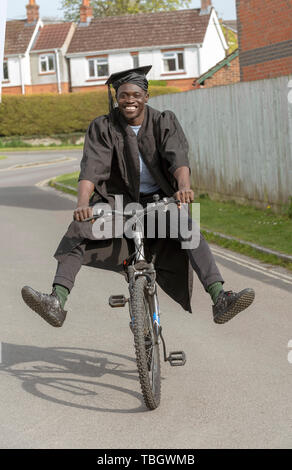 Andover, Hampshire, Inghilterra, Regno Unito. Maggio 2019. Uno studente universitario che indossa il cappello e camice in sella ad una bicicletta. Foto Stock