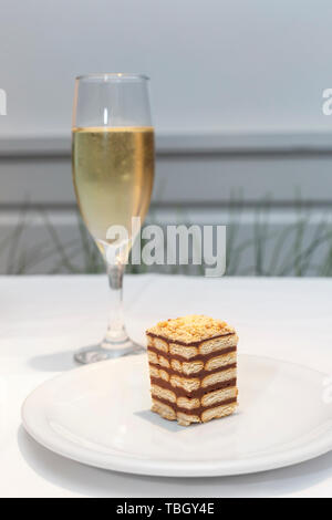 Fetta di una Torta di biscotti su una piastra bianca con vetro di dessert di vino bianco in un bicchiere da vino Foto Stock