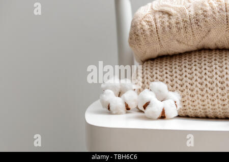 Maglioni lavorati a maglia con fiori di cotone sulla sedia bianca contro lo sfondo grigio Foto Stock