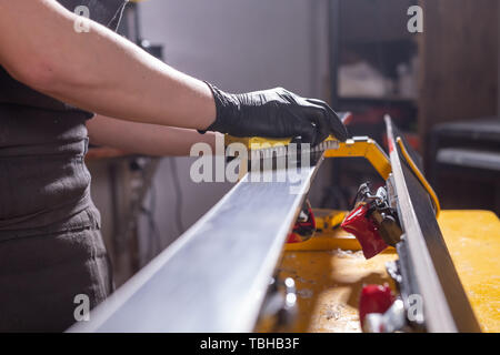 Lavoro e concetto di riparazione - un uomo con le mani in mano la riparazione sci mediante sfregamento di una paraffina Foto Stock