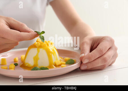 Donna decorazione di gustoso panna cotta a tavola Foto Stock