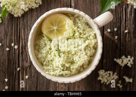 Macerazione di freschi fiori di sambuco e limone in acqua per preparare in casa lo sciroppo a base di erbe, vista dall'alto Foto Stock