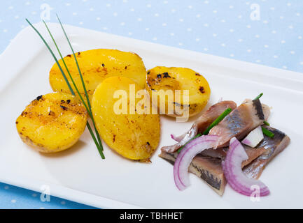 Fette di dolce-cured aringa con patate fritte e cipolle servito sulla piastra a tavola Foto Stock