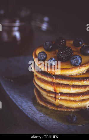 Frittelle con frutti di bosco freschi e sciroppo d'acero su sfondo scuro. American Classic colazione casalinga. Foto Stock