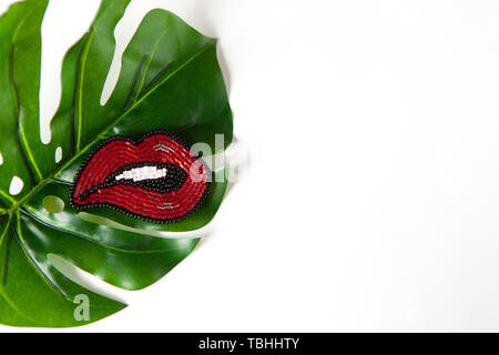 Elegante spilla a forma di labbra da perle giapponesi su verde foglia di monstera su sfondo bianco. Close-up, laici piana, copia dello spazio. Concetto tre Foto Stock