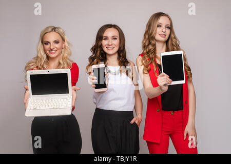 Tre signore usando i gadget. Tre bellissime elegante delle giovani donne in vestiti casual Foto Stock