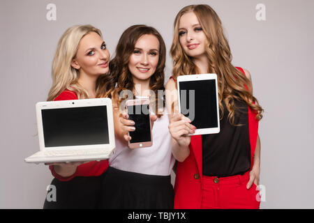 Tre signore usando i gadget. Tre bellissime elegante delle giovani donne in vestiti casual Foto Stock
