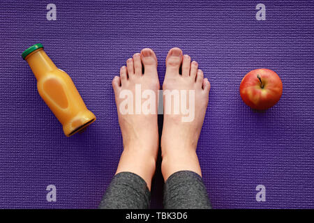 Gambe di sportivo da donna con Apple e una bottiglia di succo di frutta sul materassino yoga Foto Stock