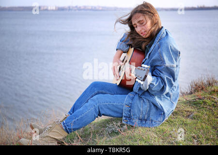 Giovane donna a suonare la chitarra vicino al fiume Foto Stock