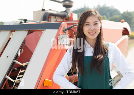 Giovane donna cinese agonomist in golden campo di cereali con piccole harvester Foto Stock