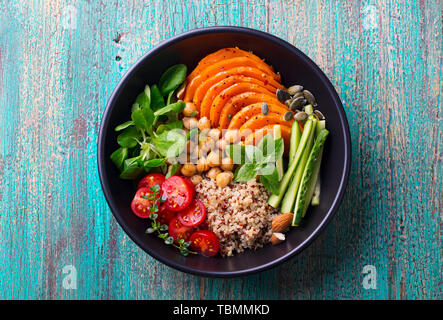 Sana insalata vegetariana. Arrosto di zucca, quinoa, pomodori, insalata verde. Ciotola di Buddha. Blu sullo sfondo di legno. Vista superiore Foto Stock