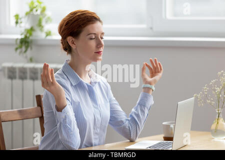 Piuttosto giovane imprenditrice meditando, facendo esercizi di respirazione in ufficio Foto Stock