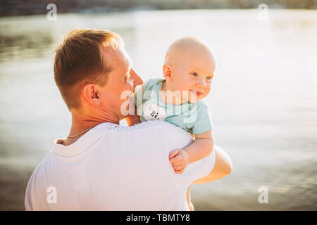 Oggetto Parenting, vacanze estive, padre e figlio. Giovani papà caucasico detiene sui bracci, abbracci bambino affacciato sulla città Kiev e il fiume sulle banche Foto Stock