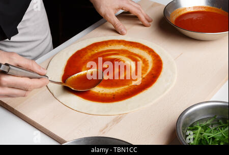 Pizza italiana preparazione. Lo Chef aggiunta di salsa a base di Pizza Foto Stock