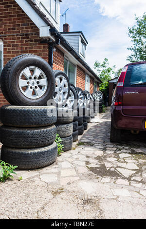 Una fila di ruote e pneumatici impilati in imposta al di fuori di un edificio in un auto scrapyard interruttori Foto Stock