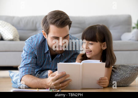 Caring papà giacente sul piano godono di lettura con piccola figlia Foto Stock