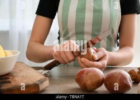 Donna di pelatura patate crudo a tavola in cucina Foto Stock