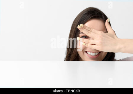 Felice giovane donna faccia del coperchio con la mano vicino a tavola su sfondo bianco Foto Stock