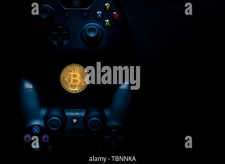 Playstation e Xbox controller accanto a un Bitcoin fisico. Foto Stock