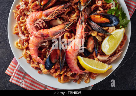 Tradizionale Fideua spagnola, un noodle Paella con frutti di mare - gamberoni, bianco carne di pesce, calamari, cozze servite su una piastra bianca su una tabella di calcestruzzo Foto Stock