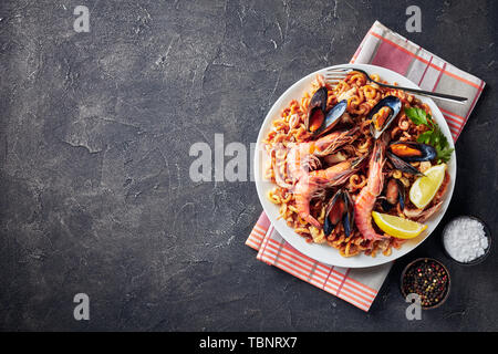 Tradizionale Fideua spagnola, un noodle Paella con frutti di mare - gamberoni, bianco carne di pesce, calamari, cozze servite su una piastra bianca su una tabella di calcestruzzo Foto Stock