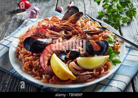 Close-up di Fideua spagnola, un noodle Paella con gamberoni, bianco carne di pesce, calamari, cozze servite su un piatto bianco su una tavola in legno rustico Foto Stock