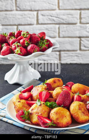 Close-up di cottage cheese ciambelle con fragole su una piastra su un tavolo di calcestruzzo. coppa di frutta con fragole fresche a sfondo nella parte anteriore di un Foto Stock