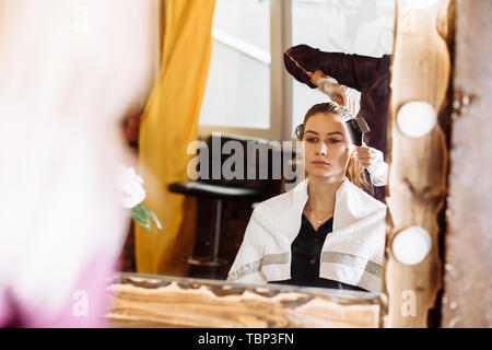 Il processo di trattamento di capelli, la colorazione dei capelli. Parrucchiere è morente capelli femmina. Bella client attraente seduti davanti ad uno specchio in elegante beaut Foto Stock