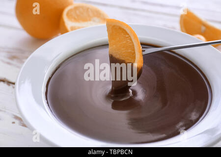 Immersione di gustoso arancione nella ciotola con la fonduta di cioccolato su tavola Foto Stock