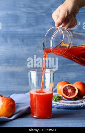 Donna versando sangue fresco succo di arancia dalla brocca in vetro sul tavolo Foto Stock