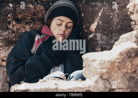 Poveri senzatetto donna seduta vicino a parete all'aperto Foto Stock