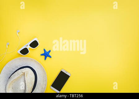 La vacanza estiva di sfondo - cappello di paglia, occhiali da sole e smart phone su sfondo giallo= Foto Stock
