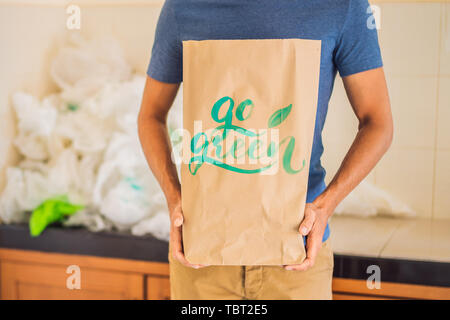 L'uomo tenendo un pacchetto con la scritta go green in mezzo a una pila di sacchi di plastica. Rifiuti Zero concetto. Il concetto di Giornata Mondiale dell Ambiente Foto Stock