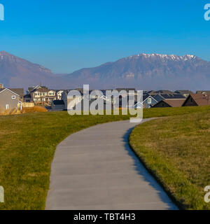 Cornice quadrata strada lastricata su una lussureggiante collina erbosa che si affaccia su belle case in una giornata di sole Foto Stock