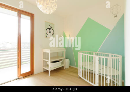 Home interni: brillante stile Scandinavo vivaio con pavimento in legno e pareti dipinte con forme geometriche in colori pastello Foto Stock