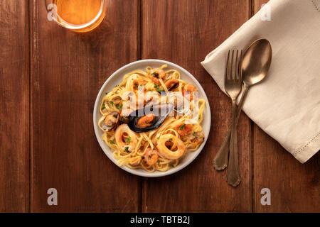 Piatti di pasta. Tagliolini con cozze, gamberi, vongole e anelli di totano, con un bicchiere di vino, girato dalla parte superiore al buio su un rustico sfondo di legno Foto Stock