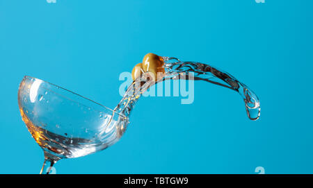 Martini con le olive verdi si riversa fuori del vetro. Sfondo blu. Copia dello spazio per il tuo testo. Foto Stock