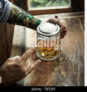 L uomo dando un diavolo gesto avvisatore acustico per heavy metal e rock and roll music mentre beve birra presso un pub o taverna in formato quadrato di un partito o festiva Foto Stock